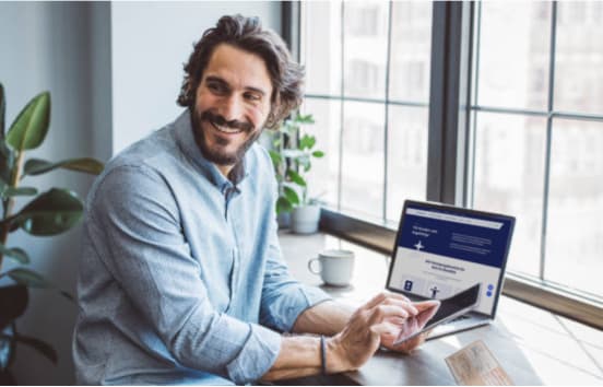 Ein Mann sitzt am Schreibtisch vor dem Labtop mit einem Tablet in der Hand. Ein Mann sitzt am Schreibtisch vor dem Labtop mit einem Tablet in der Hand.